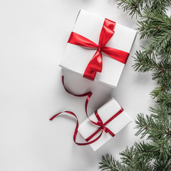 Creative frame made of Christmas fir branches on white paper background with red decoration, gift boxes. Xmas and New Year theme. Flat lay, top view