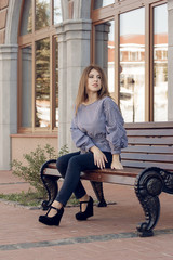 Young black woman with afro hairstyle sitting on a bench in urban background moving her legs. Mixed girl wearing casual clothes.