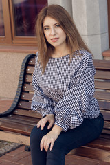 Young black woman with afro hairstyle sitting on a bench in urban background moving her legs. Mixed girl wearing casual clothes.