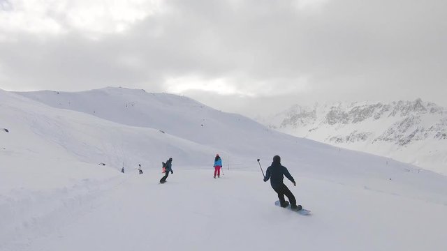 Snowboarder filming his ski and snowboard friends with a selfiestick on a cloudy day