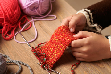 Child boy is learning to knit. Colorful wool yarns are on the wooden table. Hand closeup.