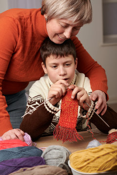 Mother is learning her child boy to knit. Colorful wool yarns are on the wooden table.