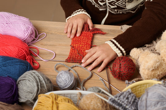 Child boy is learning to knit. Colorful wool yarns are on the wooden table. Hand closeup.