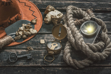 Compas, gold nuggets on the spade, rope and flashlight on the aged wooden table background. Treasure hunter or goldminer concept.