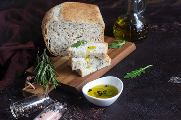 Sliced fresh bread and extra virgin olive oil on dark brown background 