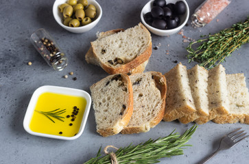 Bread, olive pepper oil, olives and rosemary on grey stone background. Top view, copy space