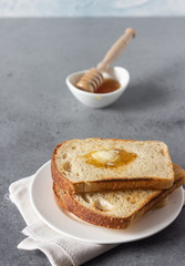 Slices of toast bread and butter with honey on grey stone background