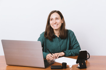 Beautiful young smiling lady working at laptop in office and looking away