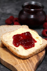 Toast bread with homemade raspberry jam or marmalade on rustic table served with butter for breakfast or brunch