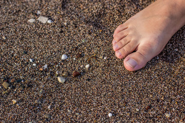 child girl bare feet on sea sand and small stones background material texture of waterfront shoreline 