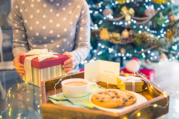 No face young woman opening Christmas present box with blurred wooden tray with festive breakfast. Cocoa and cookies for Santa. Christmas and New Year background. Soft selective focus. Vintage tonning