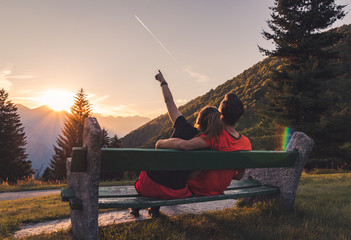 Couple sitting on bench in the mountains watching the sunset and a plane flying