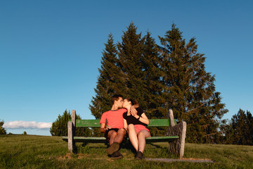 Couple in love sitting on bench in the mountains and kissing after a hike