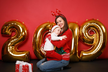 Merry Santa boy mom in Christmas hat celebrating holiday party isolated on bright red wall background golden shiny glitter numbers air balloons full length studio portrait. Happy New Year 2019 concept