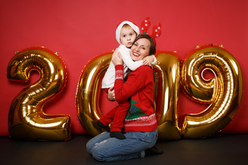 Merry Santa boy mom in Christmas hat celebrating holiday party isolated on bright red wall background golden shiny glitter numbers air balloons full length studio portrait. Happy New Year 2019 concept