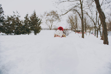 Pretty little girl in winter warm clothes and hat playing, hiding behind snowball in snowy park or forest outdoors. Winter fun, leisure on holidays. Love relationship family people lifestyle concept.