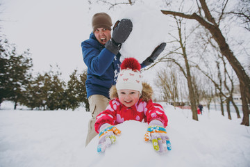 Funny family screaming dad in warm clothes holding big snowball, little girl playing with snow in park or forest outdoors. Winter fun, leisure on holidays. Love relationship family lifestyle concept.