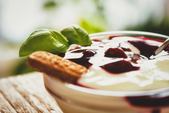 Rote Gr&uuml;tze mit Joghurt bei Tageslicht auf Holztisch