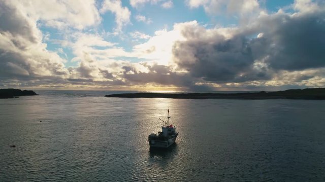 Stunning Aerial Drone Shot in Scottish Highlands, looking out to sunset at sea, flyover one small fishing boat off Portnahaven on the Isle of Islay