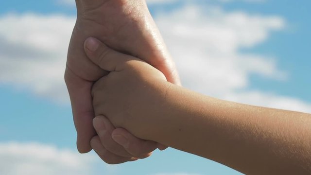 Parent holds the hand of a child. Mother holds the hand of the child against the blue sky.