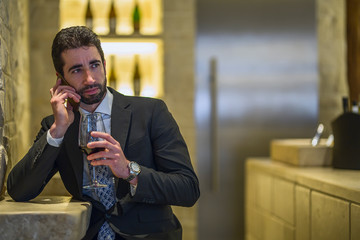 Young man talking on the phone while drinking wine at the bar
