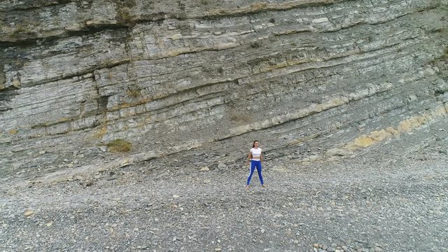 Woman is doing squats the bodyflex during breathing exercises on the rock background. Aerial beautiful footage view.