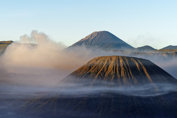 View in the morning light on a volcanic mountain surrounded by clouds and fog with strongly...