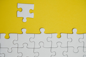 Fototapeta premium Fragment of a folded white jigsaw puzzle and a pile of uncombed puzzle elements against the background of a yellow surface.