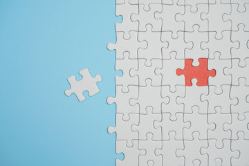 Fragment of a folded white jigsaw puzzle and a pile of uncombed puzzle elements against the background of a blue surface.