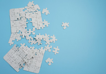 Fragment of a folded white jigsaw puzzle and a pile of uncombed puzzle elements against the...
