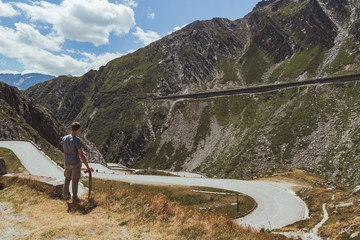 young man with longboard contemplating a curvy road descending in a valley - Powered by Adobe