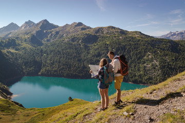 Young couple with backpack reading a map in the swiss alps. Lake ritom as background