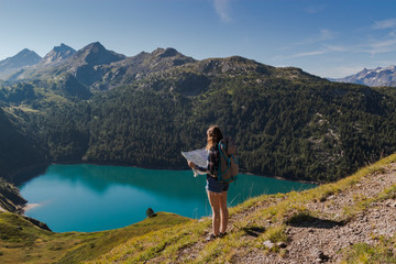 Naklejka na ściany i meble Young woman with backpack reading a map in the swiss alps. Lake ritom as background