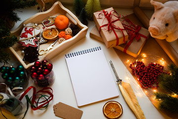 Naklejka na ściany i meble A rectangular white notebook on a white background surrounded by pigs and Christmas and New Year trifles, balls, oranges, fountain pen, gifts in Kraft paper, packing tape, garlands.