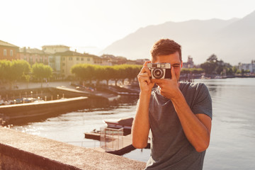 young man using a vintage camera in front of the lake promenade in Ascona