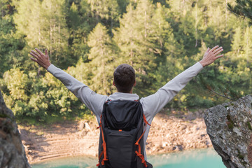 Young man with backpack and arms raised enjoying freedom in the mountains during a sunny day