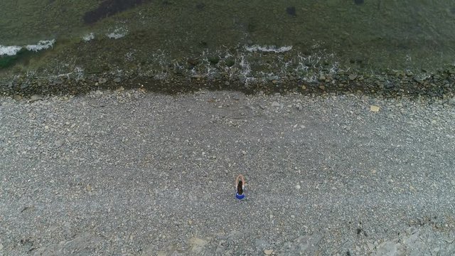 Woman is doing squats the bodyflex on the sea stone beach. Aerial beautiful footage top view.