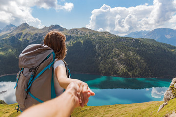 follow me concept of young woman with a big backpack in the mountains looking at the lake