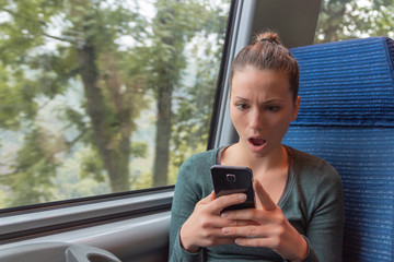 Amazed woman checking smartphone in the street after receiving a shocking news on a train journey