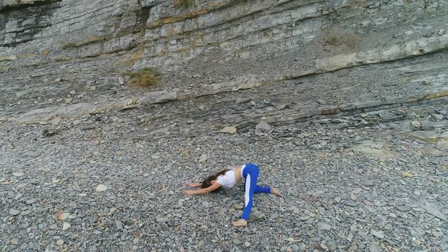 Woman is doing yoga and stretcing bodyflex exercises on rock and sea background. Aerial beautiful footage side view.