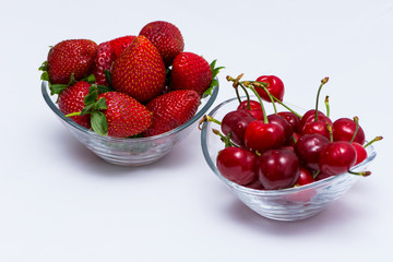 One bowl full of cherry and one bowl full of strawberries