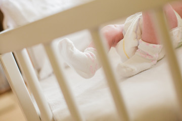 Legs of baby on the background of white sheets. The baby is lying in the crib among the pillows.