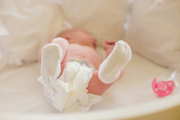 Obraz na płótnie Canvas Legs of baby on the background of white sheets. The baby is lying in the crib among the pillows. Soft focus