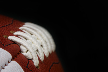 An American football game ball is shown up close, with the focus showing the detail of the laces,...