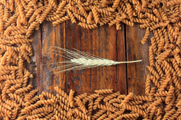 Top view of raw wholemeal pasta from Fusilli, on a wooden background with wheat boughs