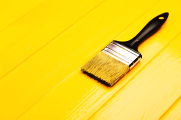 Paintbrush with black handle on yellow freshly painted wooden background. Repairing concept....