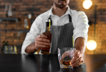 Bartender with glass and bottle of whiskey at counter in bar, closeup. Space for text