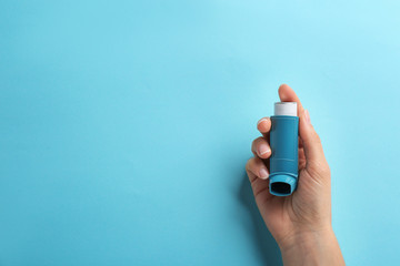 Woman holding asthma inhaler on color background, top view. Space for text