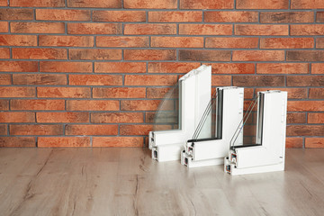 Samples of modern window profiles on floor against brick wall, space for text. Installation service