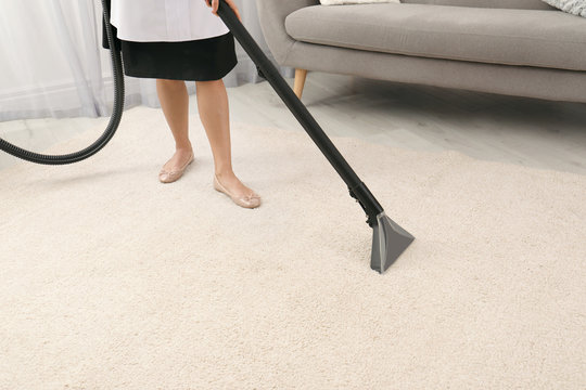 Chambermaid removing dirt from carpet with vacuum cleaner indoors, closeup. Space for text
